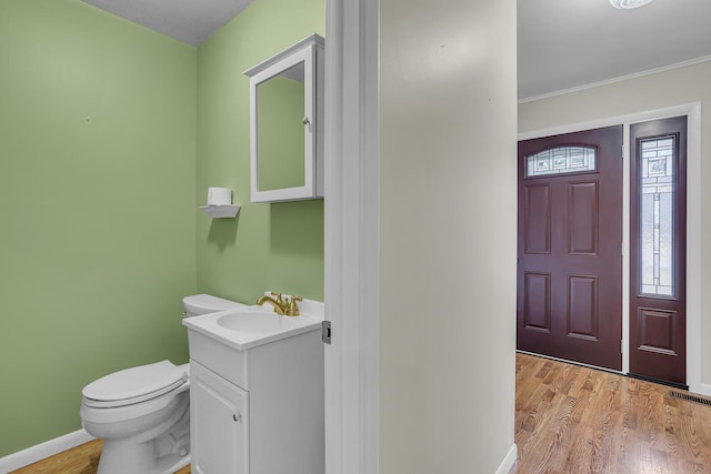 half bath featuring vanity, wood finished floors, toilet, and baseboards