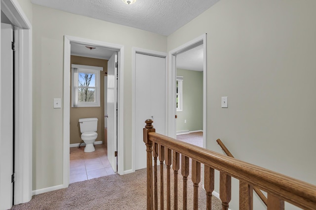 hallway with light colored carpet, light tile patterned flooring, a textured ceiling, an upstairs landing, and baseboards