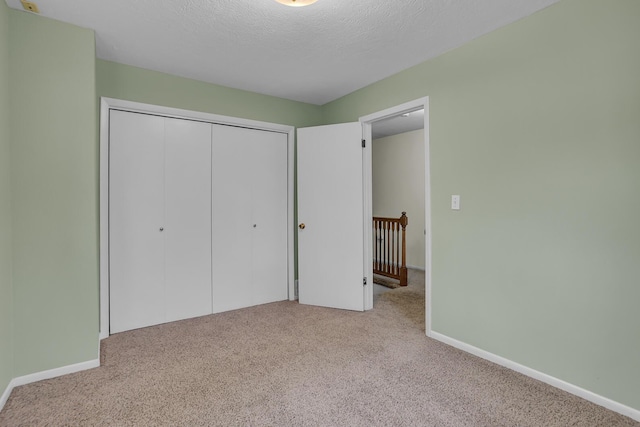 unfurnished bedroom with a closet, a textured ceiling, baseboards, and carpet flooring