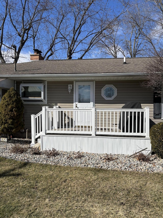 doorway to property with a shingled roof, covered porch, a lawn, and a chimney