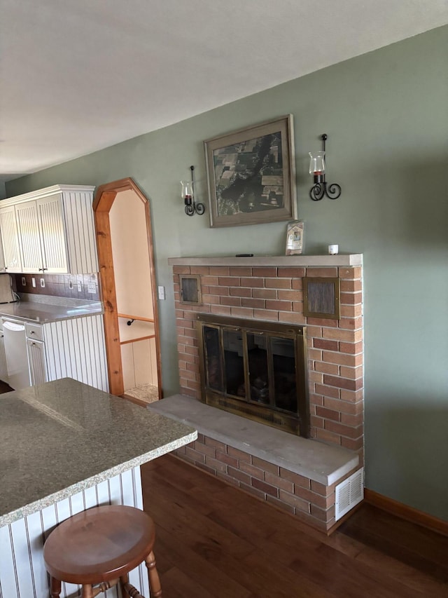 living room with a brick fireplace, visible vents, baseboards, and wood finished floors