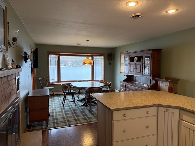 kitchen with visible vents, dark wood-style flooring, light countertops, white cabinets, and a glass covered fireplace