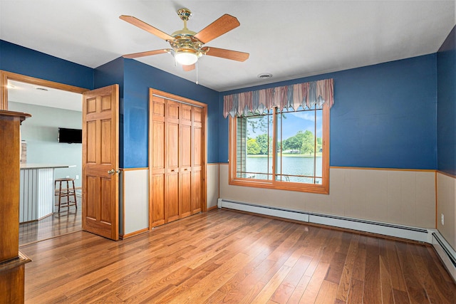 222 Crockett Dr, Quincy, MI 49082 - unfurnished bedroom featuring light wood-type flooring, wainscoting, a closet, a baseboard radiator, and a ceiling fan