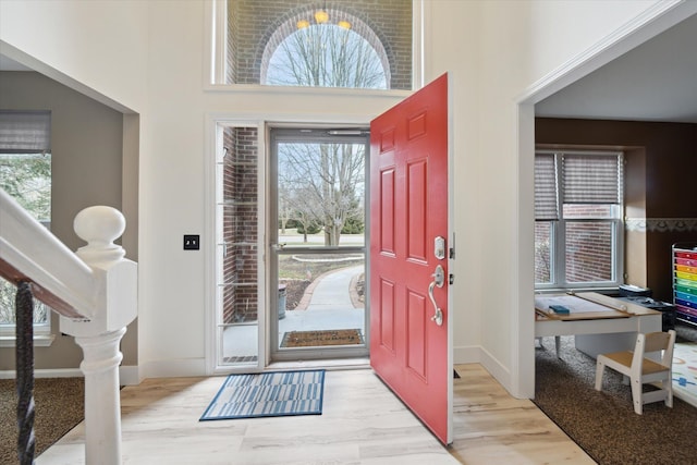 foyer entrance with light wood-style flooring, a high ceiling, and baseboards