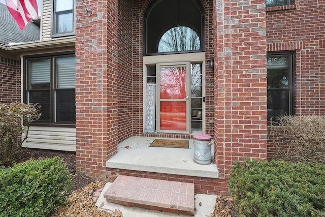 view of exterior entry with brick siding and roof with shingles