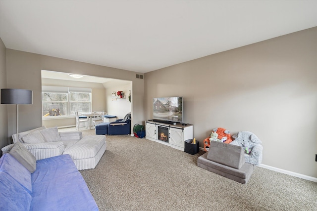 carpeted living area featuring baseboards, visible vents, and a lit fireplace