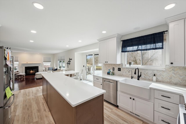 kitchen with a kitchen island, decorative backsplash, appliances with stainless steel finishes, a glass covered fireplace, and a sink