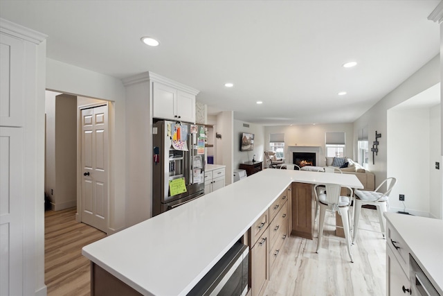 kitchen featuring fridge with ice dispenser, a center island, recessed lighting, a lit fireplace, and light countertops