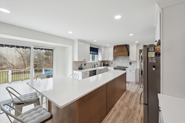 kitchen featuring premium range hood, light countertops, decorative backsplash, light wood-style flooring, and appliances with stainless steel finishes