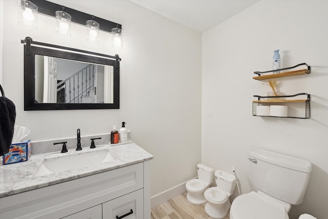 bathroom featuring baseboards, toilet, a bidet, wood finished floors, and vanity