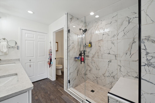 bathroom with a marble finish shower, double vanity, wood finished floors, and a sink