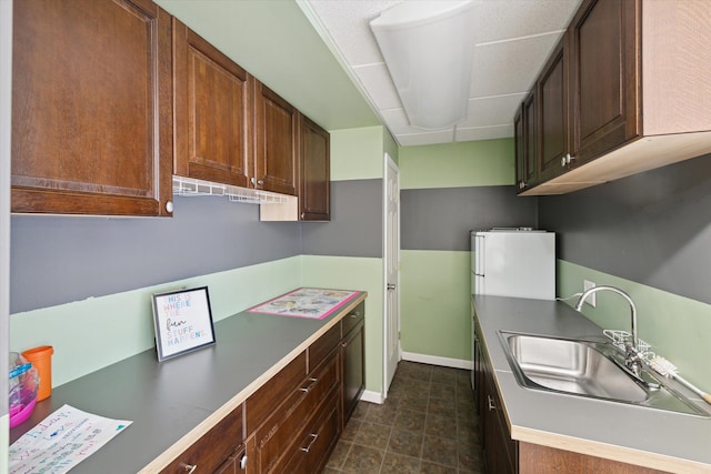 kitchen featuring refrigerator, baseboards, and a sink