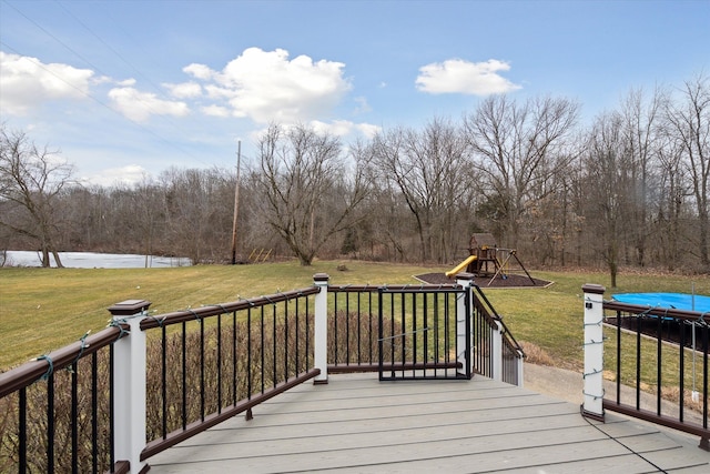 wooden terrace featuring a forest view, a water view, a playground, a trampoline, and a lawn