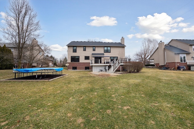 rear view of property featuring a yard, a trampoline, a wooden deck, and stairs