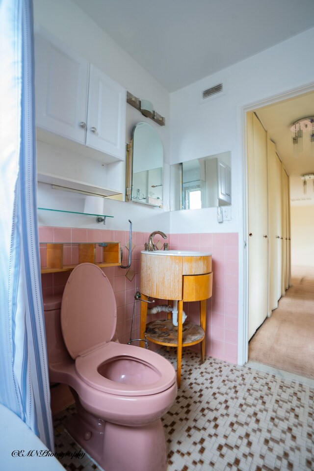 bathroom featuring visible vents, toilet, a wainscoted wall, vanity, and tile walls