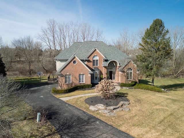 traditional-style house featuring brick siding, aphalt driveway, a front lawn, and roof with shingles