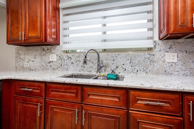 kitchen featuring reddish brown cabinets, a sink, light stone countertops, and decorative backsplash