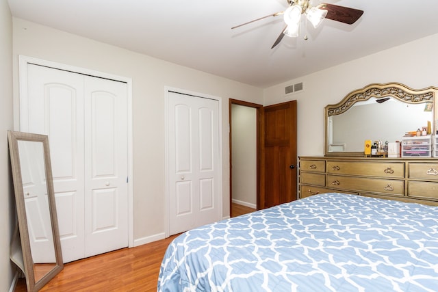 bedroom featuring a ceiling fan, baseboards, multiple closets, visible vents, and light wood-style floors