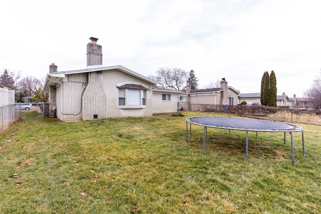 rear view of house featuring a fenced backyard, brick siding, a lawn, a trampoline, and a chimney