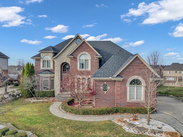 view of front of house featuring a front yard, brick siding, and roof with shingles