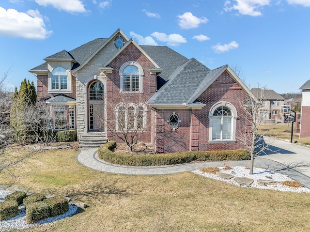 view of front facade with brick siding, stone siding, a shingled roof, and a front lawn