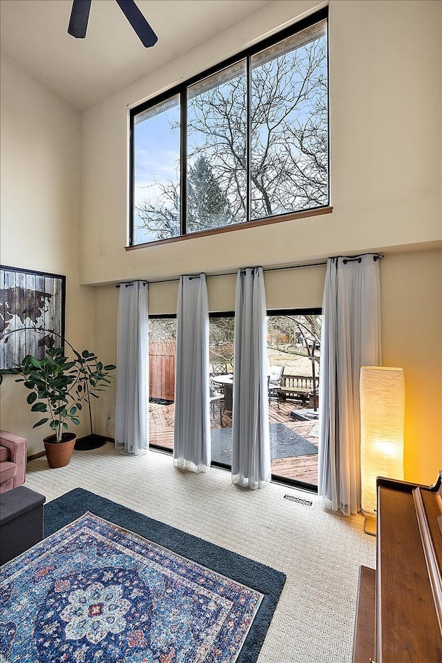 carpeted living room featuring a high ceiling, plenty of natural light, visible vents, and ceiling fan