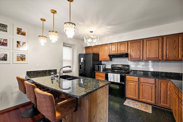 kitchen with a sink, black appliances, under cabinet range hood, a kitchen breakfast bar, and brown cabinets