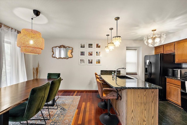 kitchen with brown cabinets, dark wood-type flooring, a breakfast bar, a sink, and dark stone countertops