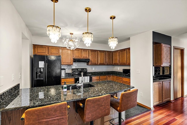 kitchen with black appliances, under cabinet range hood, a kitchen breakfast bar, decorative backsplash, and dark wood-style flooring