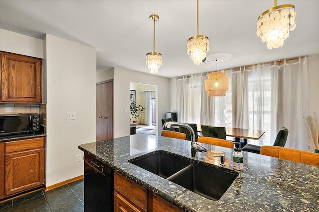 kitchen featuring dark stone countertops, brown cabinetry, a sink, black appliances, and pendant lighting