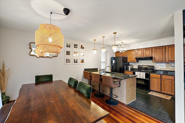 kitchen with black appliances, a breakfast bar, under cabinet range hood, a peninsula, and brown cabinetry