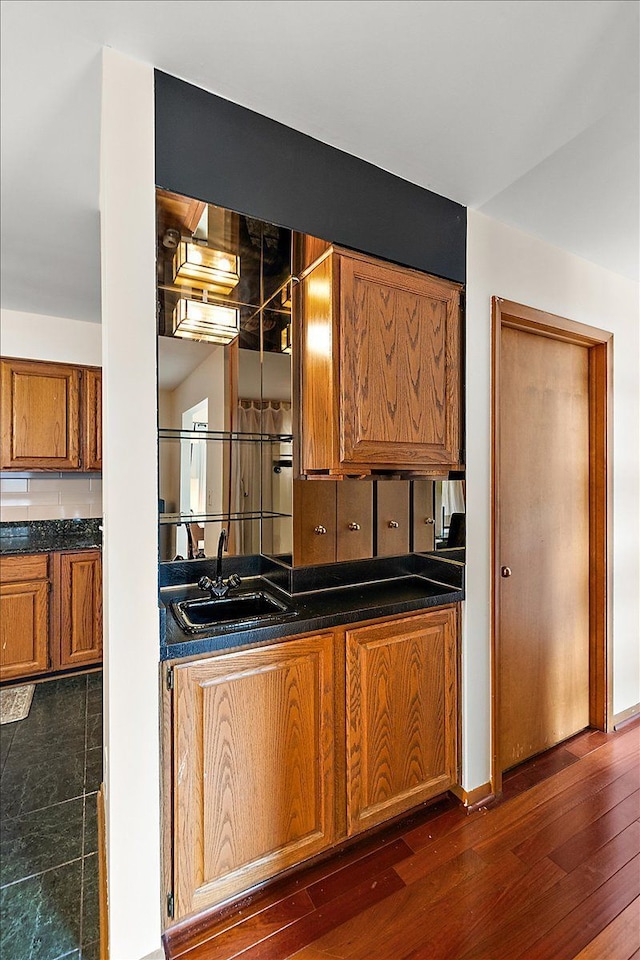 kitchen with brown cabinetry, dark wood finished floors, dark countertops, and a sink