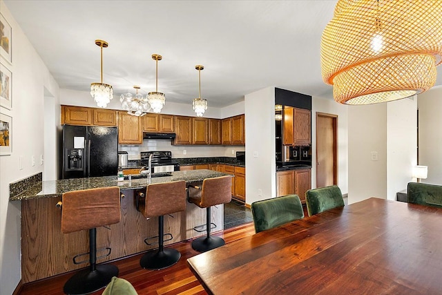 kitchen featuring black appliances, dark countertops, under cabinet range hood, and a sink