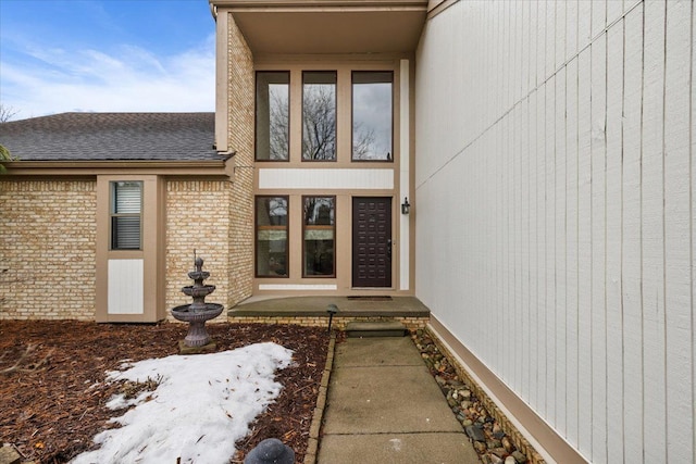 doorway to property with brick siding and roof with shingles