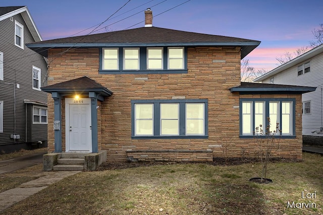 view of front of property featuring stone siding, a chimney, a front lawn, and roof with shingles