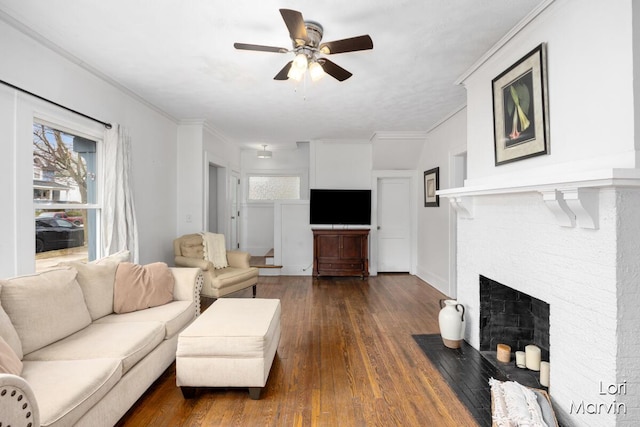 living room with baseboards, dark wood finished floors, a ceiling fan, ornamental molding, and a brick fireplace