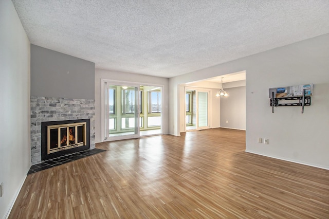 unfurnished living room with a notable chandelier, a fireplace, a textured ceiling, and wood finished floors