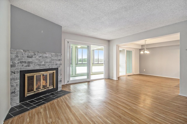 unfurnished living room with a chandelier, a brick fireplace, baseboards, and wood finished floors