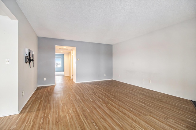 empty room featuring light wood-type flooring, a textured ceiling, and baseboards