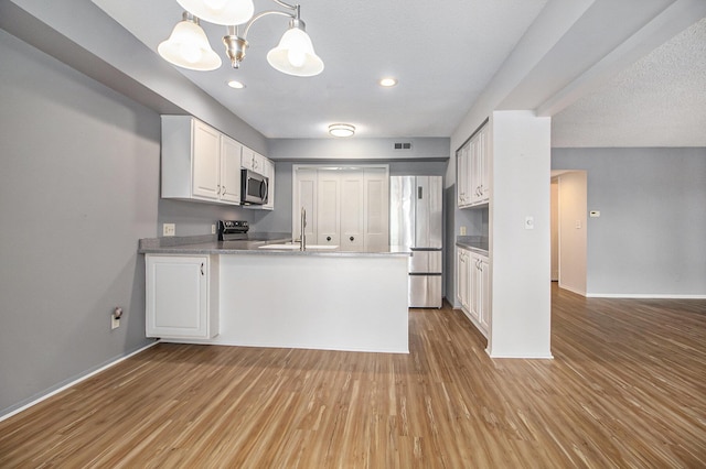 kitchen with a chandelier, stainless steel appliances, wood finished floors, and white cabinetry