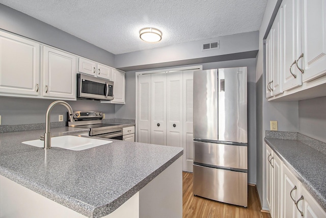 kitchen with visible vents, light wood-style flooring, appliances with stainless steel finishes, white cabinetry, and a sink