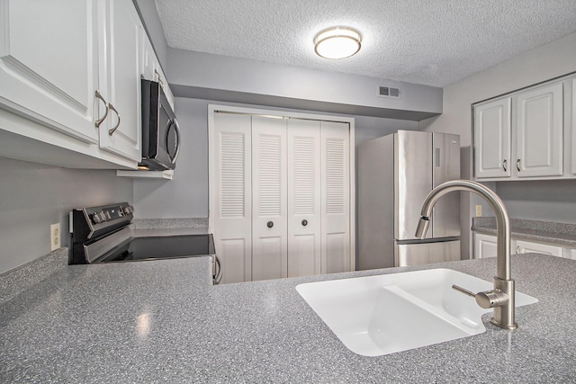 kitchen featuring a textured ceiling, stainless steel appliances, a sink, visible vents, and white cabinetry