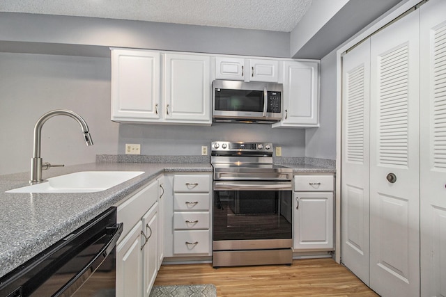 kitchen with appliances with stainless steel finishes, white cabinetry, a sink, and light wood-style flooring