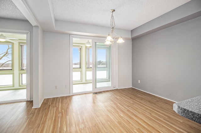 empty room with visible vents, light wood-style floors, a textured ceiling, baseboards, and ceiling fan with notable chandelier