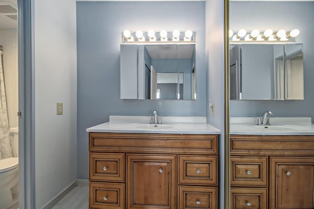 full bath with baseboards, a sink, toilet, and double vanity