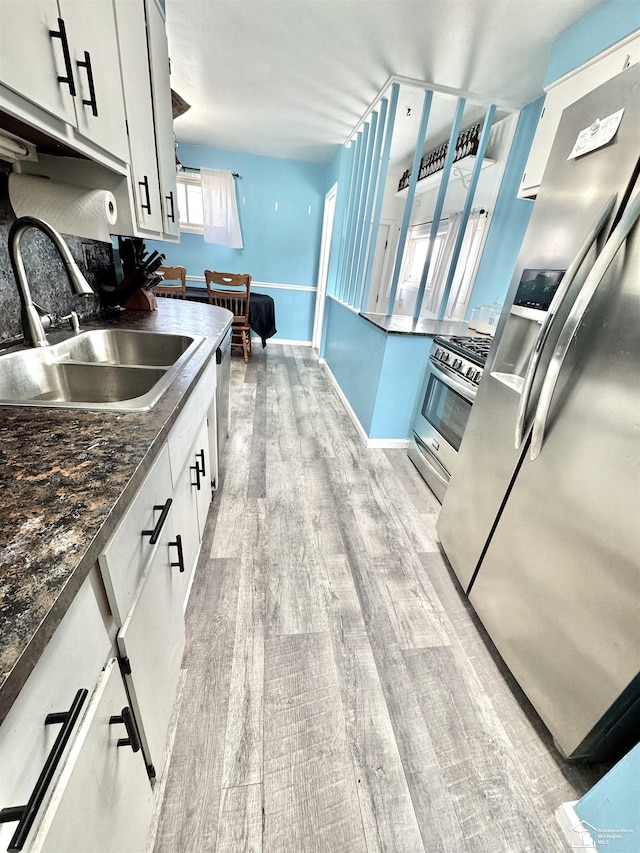 kitchen featuring light wood-style flooring, a sink, white cabinetry, appliances with stainless steel finishes, and dark countertops