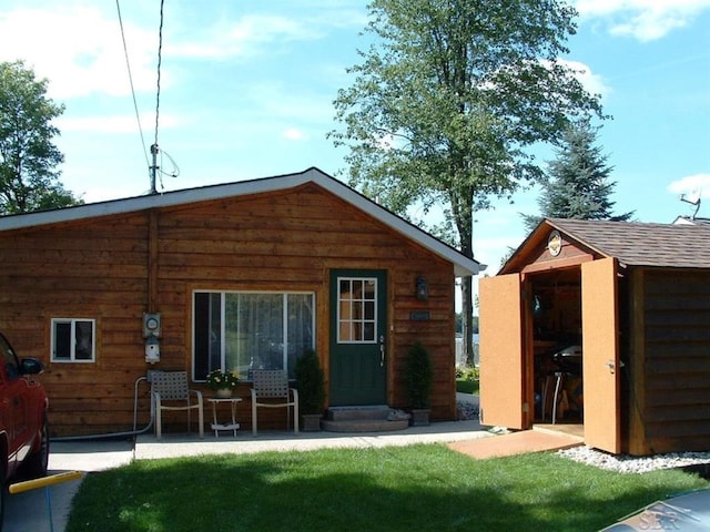 back of house featuring roof with shingles, a lawn, and an outdoor structure