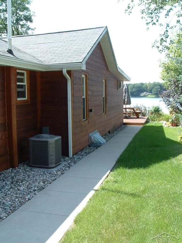 view of side of property with a water view, a shingled roof, central AC unit, and a lawn