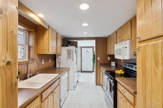 kitchen featuring dark countertops, white appliances, light tile patterned floors, and a sink