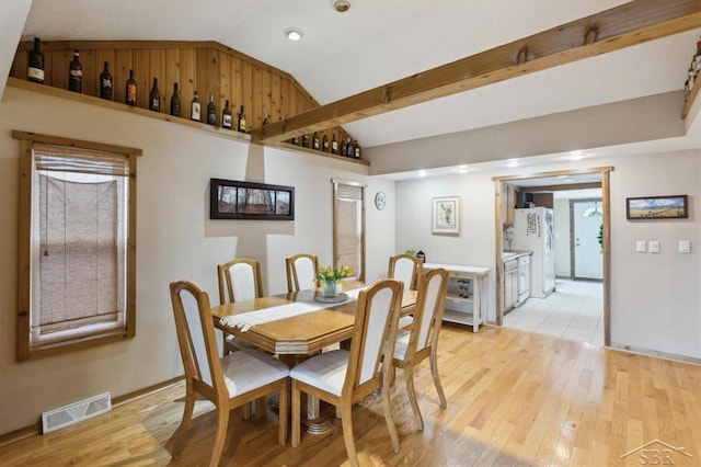 dining area featuring light wood-type flooring, visible vents, and vaulted ceiling with beams